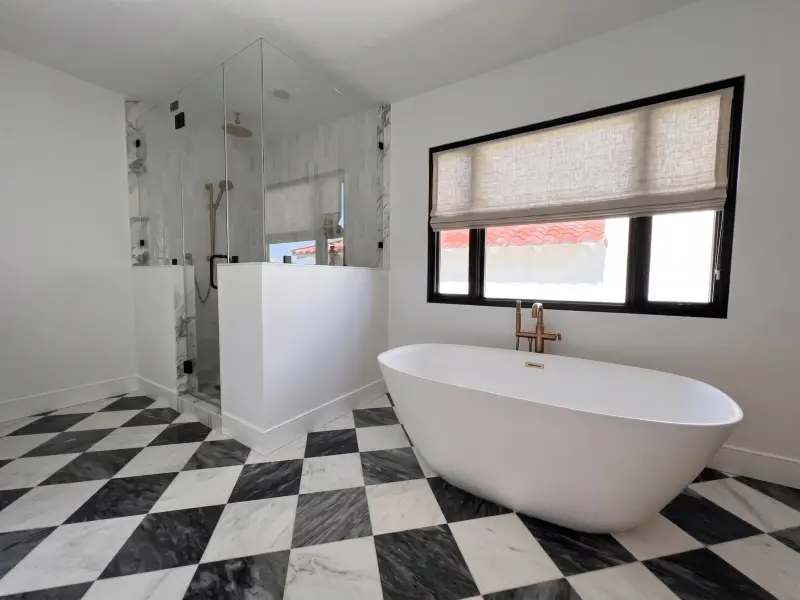 Freestanding tub on a black and white checkerboard floor beside a glass shower