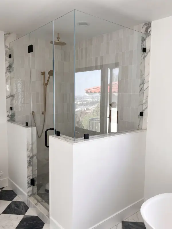 Frameless glass shower with marble-look trim and a brass rain head